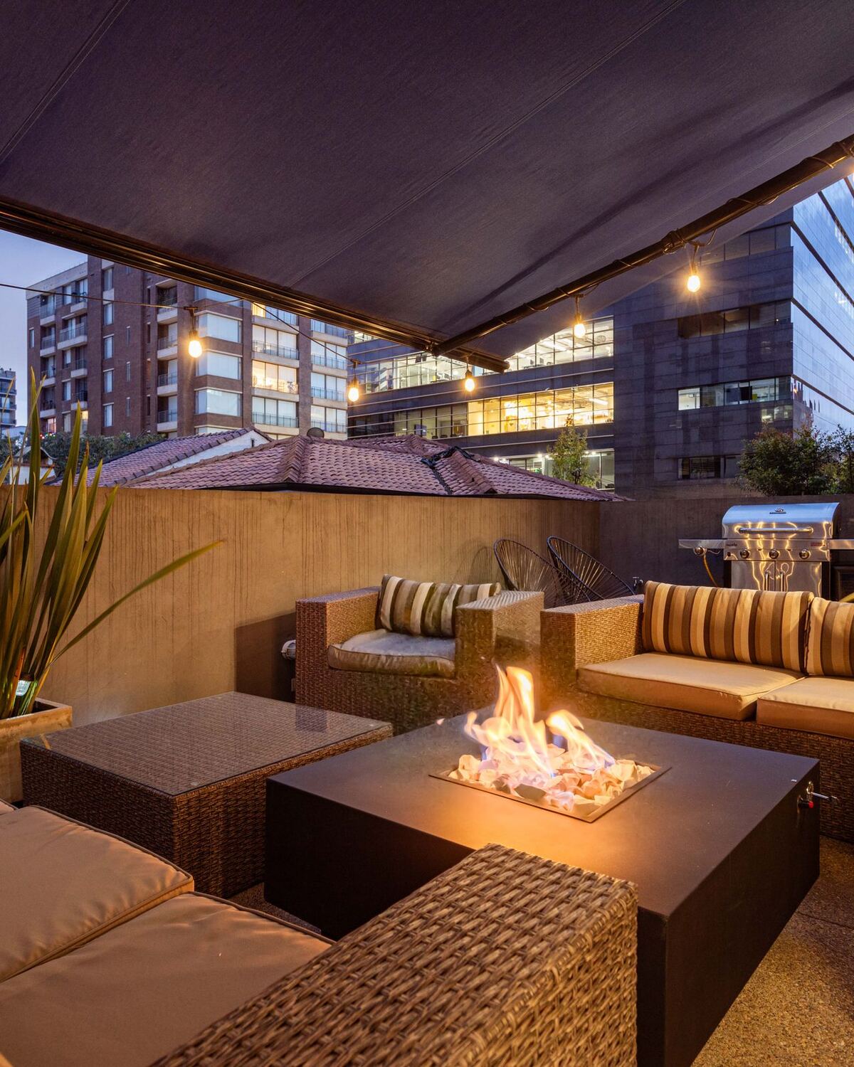 Sunken stone seating area with a fire table, pleached trees and warm evening lighting